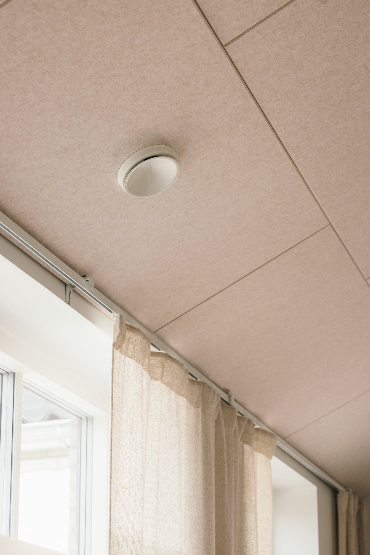 Arku rektangulært akustikpanel i lys sand. I moderne bolig monteret i loft til kip tilpasset til ventilationskanal tæt på vinduer med gardiner.